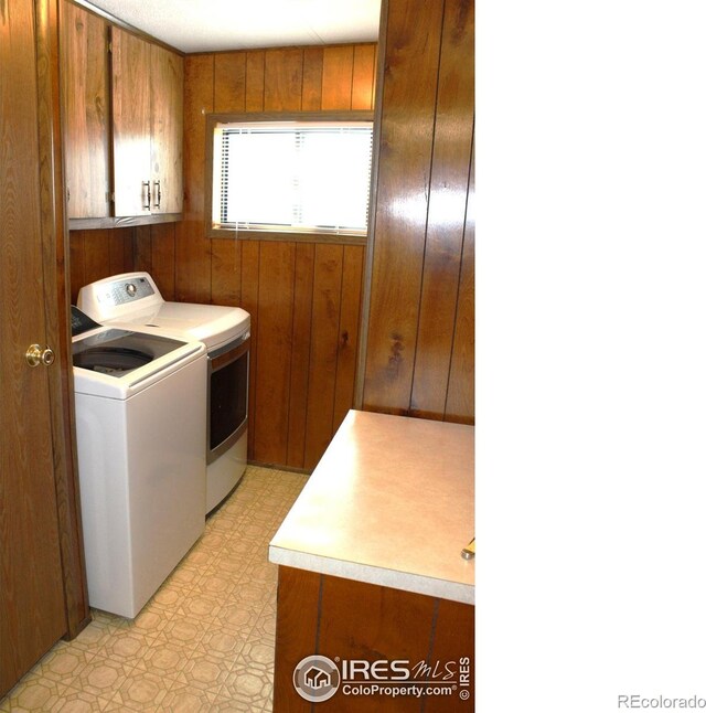 washroom with cabinets, wooden walls, and separate washer and dryer