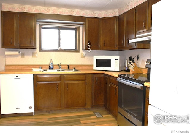 kitchen featuring a sink, light wood-style floors, white appliances, light countertops, and under cabinet range hood
