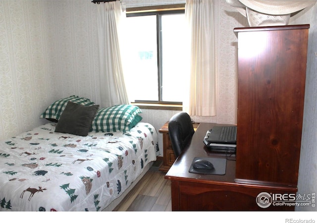 bedroom featuring wood finished floors, multiple windows, and wallpapered walls