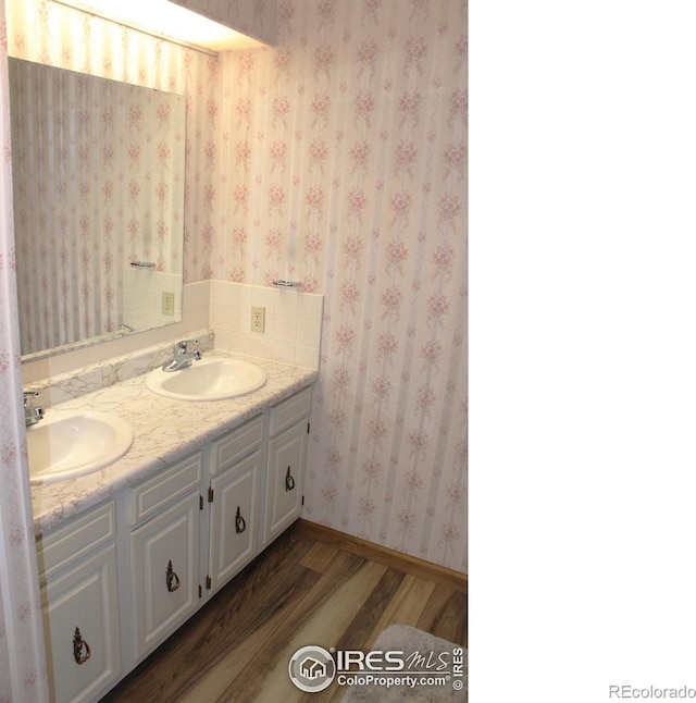 full bath featuring double vanity, wallpapered walls, a sink, and wood finished floors