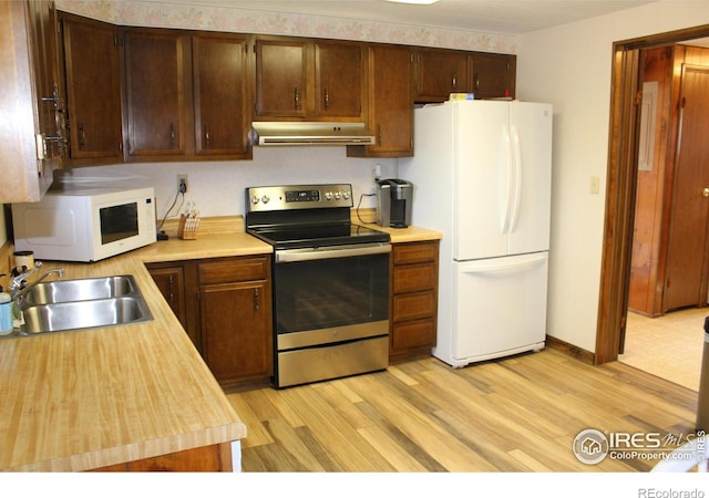 kitchen with a sink, light countertops, light wood-style floors, under cabinet range hood, and white appliances