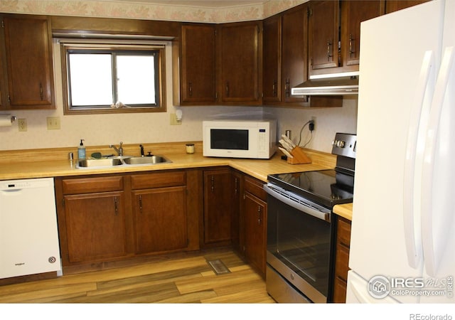 kitchen with a sink, light countertops, under cabinet range hood, and white appliances