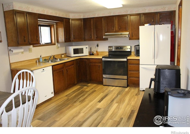 kitchen featuring white appliances, light wood-style floors, light countertops, under cabinet range hood, and a sink