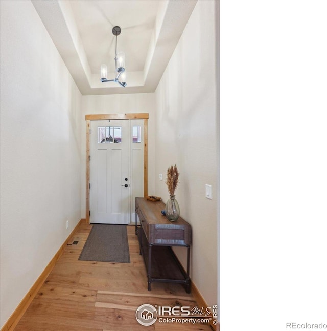 entryway with hardwood / wood-style floors, a raised ceiling, and a chandelier