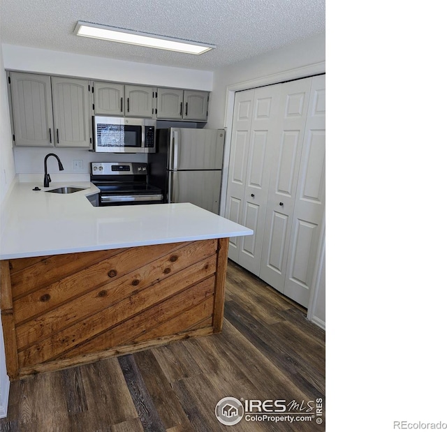 kitchen featuring sink, stainless steel appliances, dark hardwood / wood-style floors, a textured ceiling, and kitchen peninsula