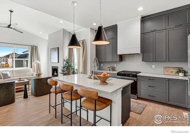 kitchen with an island with sink, backsplash, a large fireplace, lofted ceiling, and black range with gas cooktop