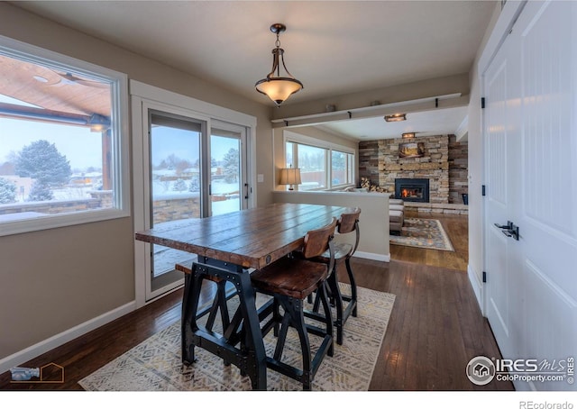 dining room with dark wood-type flooring and a stone fireplace