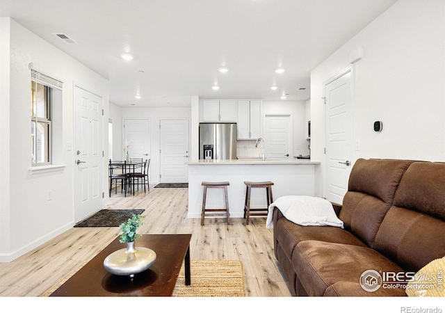 living room with baseboards, light wood-style flooring, visible vents, and recessed lighting