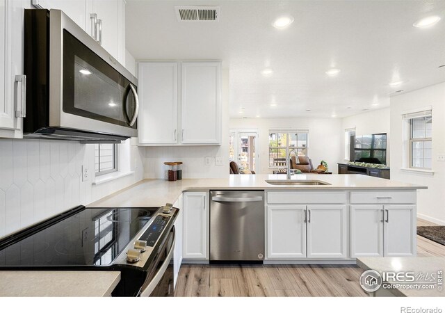 kitchen featuring a peninsula, white cabinetry, appliances with stainless steel finishes, and a sink