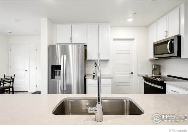 kitchen with recessed lighting, a sink, white cabinets, light countertops, and appliances with stainless steel finishes