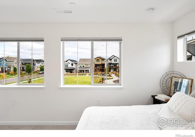 carpeted bedroom featuring a residential view, multiple windows, visible vents, and baseboards