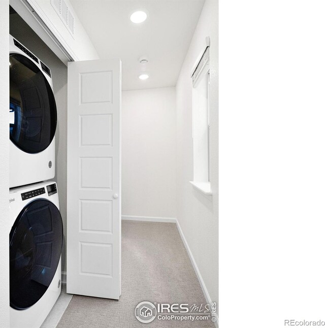 washroom with light carpet, stacked washer and dryer, laundry area, visible vents, and baseboards