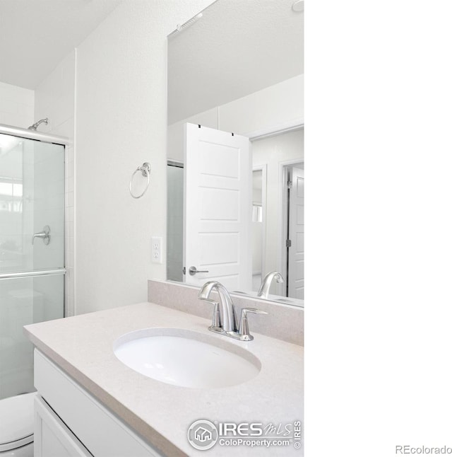 bathroom with toilet, vanity, and a shower with shower door