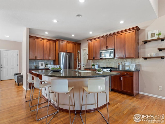 kitchen featuring light hardwood / wood-style floors, a breakfast bar area, stainless steel appliances, a kitchen island with sink, and sink