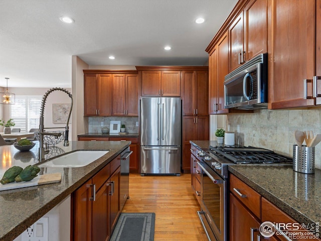 kitchen with backsplash, dark stone countertops, stainless steel appliances, and light hardwood / wood-style flooring