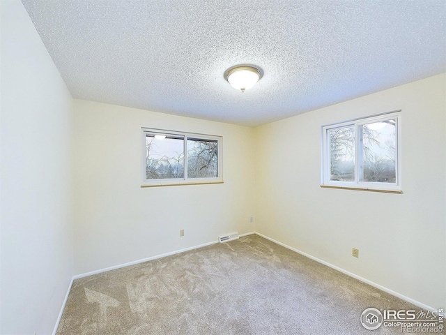 carpeted spare room featuring visible vents, baseboards, and a textured ceiling