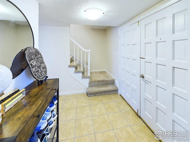 entryway featuring baseboards, a textured ceiling, light tile patterned flooring, and stairs