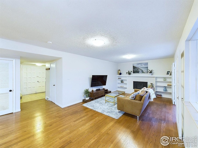 living room featuring baseboards, a textured ceiling, wood finished floors, and a fireplace