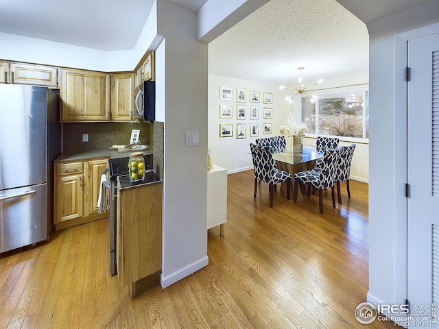 kitchen featuring baseboards, light wood-style floors, appliances with stainless steel finishes, dark countertops, and tasteful backsplash