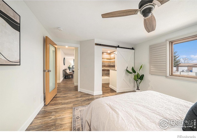 bedroom featuring ceiling fan, ensuite bathroom, a barn door, and dark hardwood / wood-style flooring