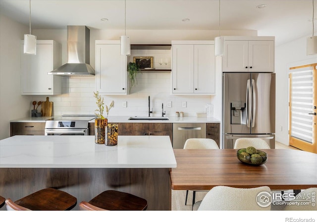 kitchen with decorative light fixtures, wall chimney range hood, sink, white cabinetry, and stainless steel appliances