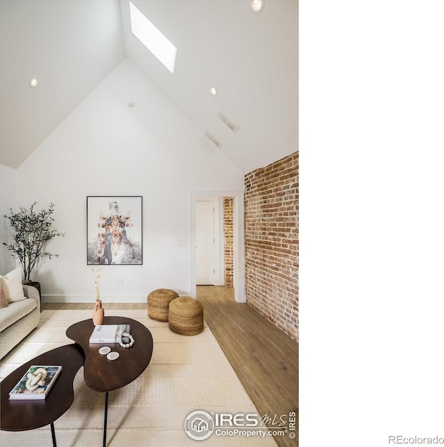 living room with high vaulted ceiling, a skylight, brick wall, and hardwood / wood-style floors