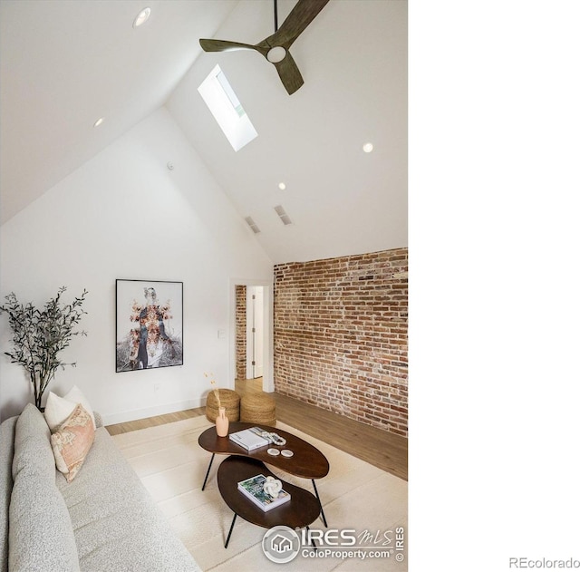 living room with brick wall, a skylight, light hardwood / wood-style floors, high vaulted ceiling, and ceiling fan