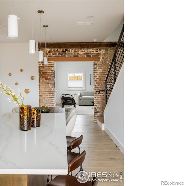 kitchen with decorative light fixtures, a kitchen breakfast bar, brick wall, and light hardwood / wood-style flooring