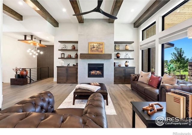 living room with beam ceiling, ceiling fan, a large fireplace, and light hardwood / wood-style floors