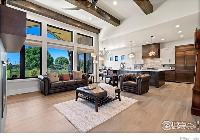 living room featuring ceiling fan with notable chandelier, sink, beam ceiling, and light wood-type flooring