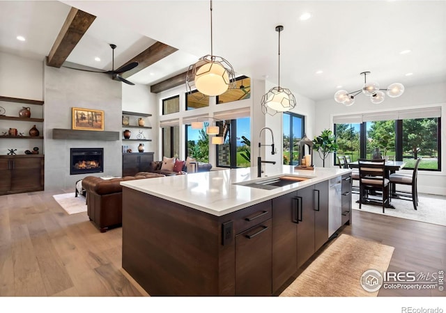 kitchen featuring a center island with sink, sink, a fireplace, dark brown cabinets, and beamed ceiling