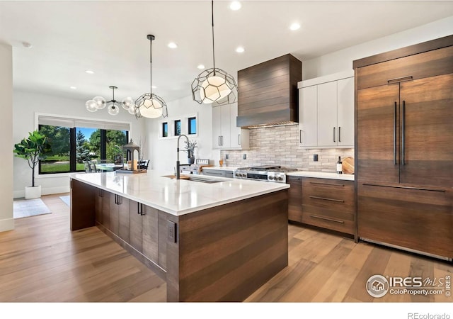 kitchen featuring a spacious island, sink, white cabinetry, custom range hood, and paneled built in refrigerator