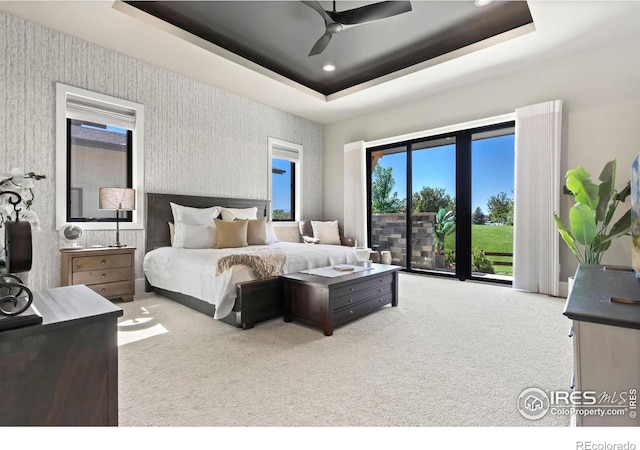 carpeted bedroom with ceiling fan, access to exterior, multiple windows, and a raised ceiling