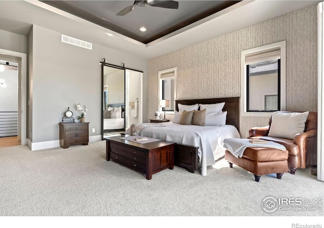 carpeted bedroom with ceiling fan, a tray ceiling, and a barn door