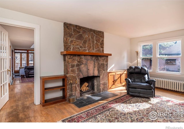 living room with wood-type flooring, radiator, and a stone fireplace