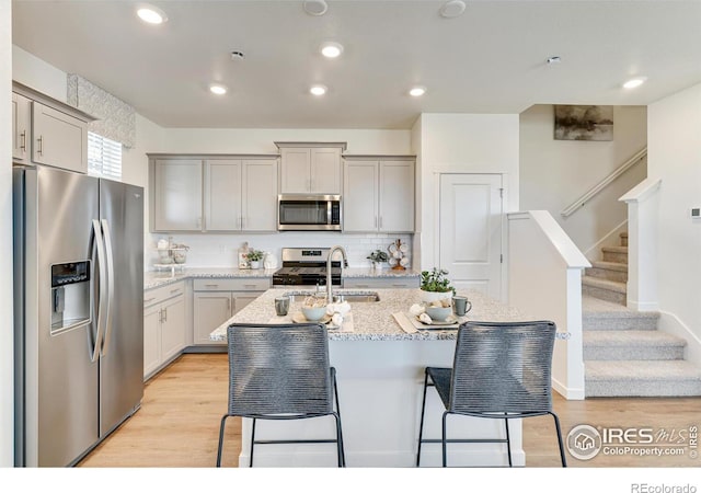 kitchen featuring gray cabinets, appliances with stainless steel finishes, tasteful backsplash, a kitchen island with sink, and light hardwood / wood-style flooring