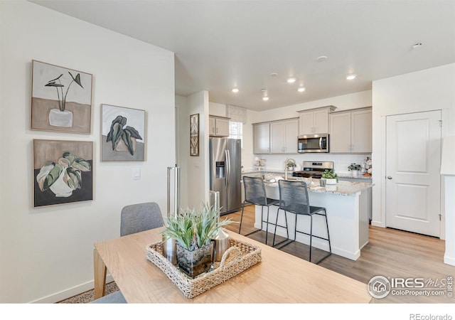 kitchen with a kitchen bar, gray cabinets, appliances with stainless steel finishes, a kitchen island with sink, and light stone counters