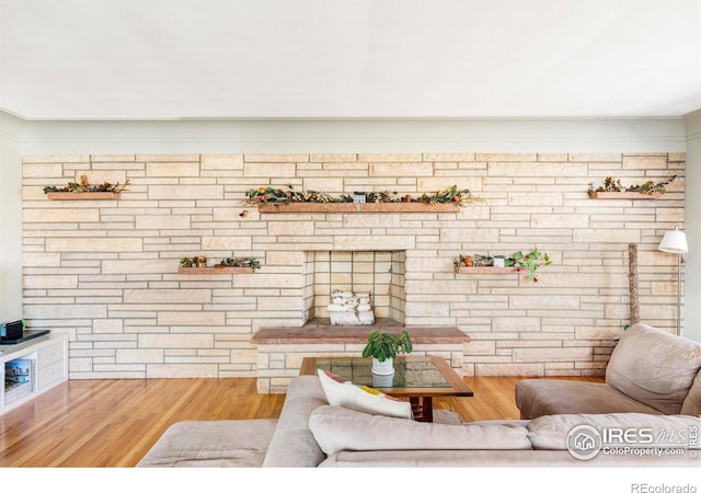 living room with wood-type flooring, brick wall, and a stone fireplace