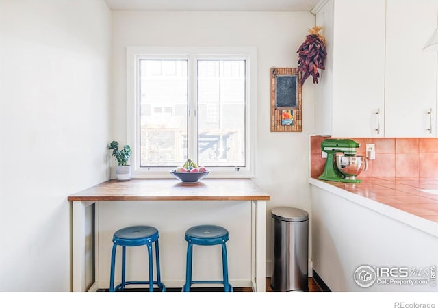 kitchen featuring a breakfast bar area, decorative backsplash, and white cabinetry