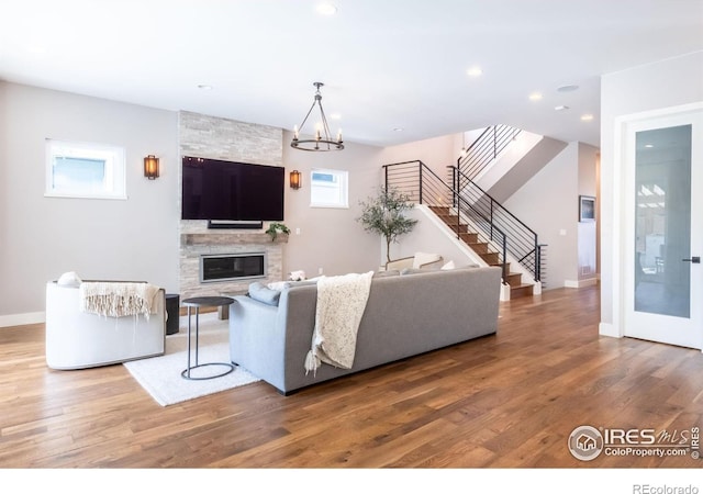 living room featuring wood-type flooring, a large fireplace, and an inviting chandelier