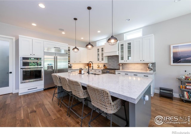 kitchen featuring a breakfast bar area, appliances with stainless steel finishes, a center island with sink, and light stone countertops