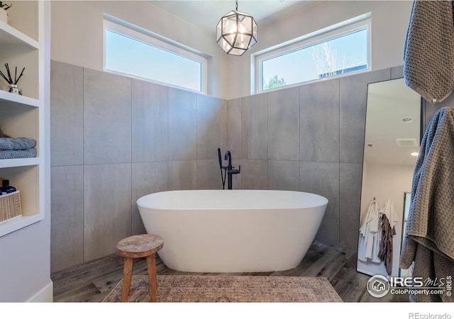 bathroom featuring built in shelves, tile walls, a bath, and hardwood / wood-style floors