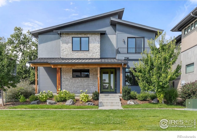 modern home with a standing seam roof, metal roof, stone siding, a balcony, and a front yard