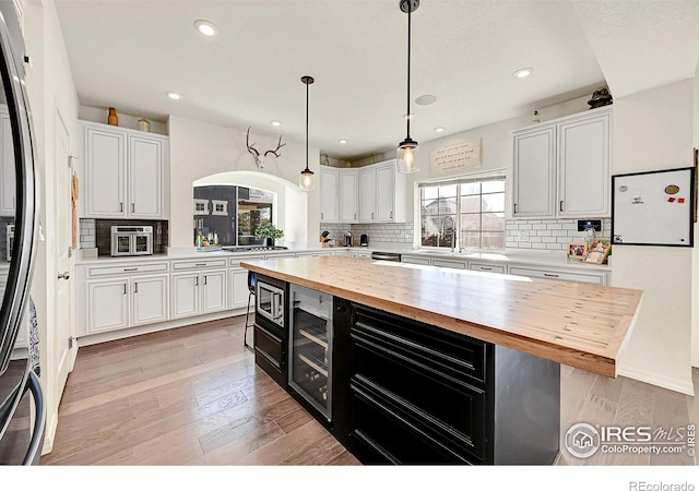 kitchen with white cabinetry, stainless steel appliances, hanging light fixtures, and wooden counters