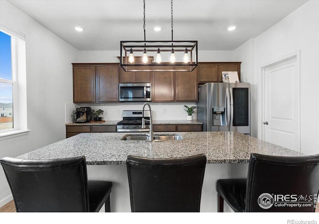 kitchen with stainless steel appliances, decorative backsplash, light stone counters, a breakfast bar, and sink