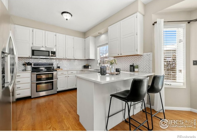 kitchen featuring a breakfast bar, stainless steel appliances, white cabinets, kitchen peninsula, and light wood-type flooring