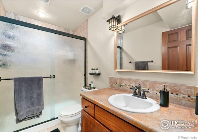 bathroom featuring tasteful backsplash, vanity, a shower with door, and toilet