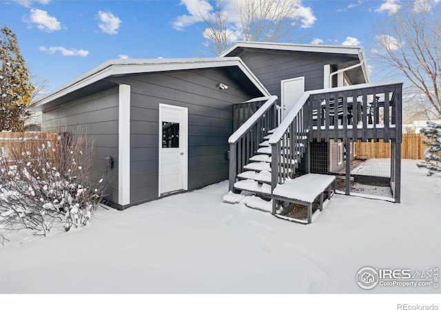 snow covered rear of property with fence, stairway, and a wooden deck