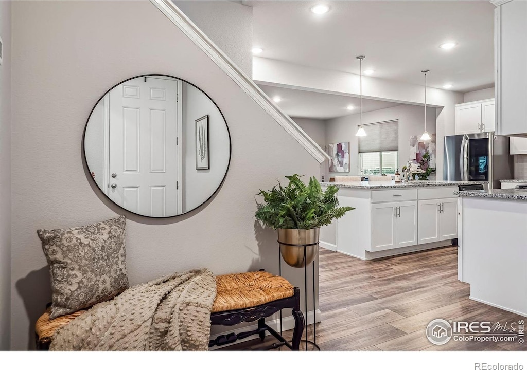 kitchen with white cabinets, decorative light fixtures, light hardwood / wood-style flooring, and stainless steel fridge