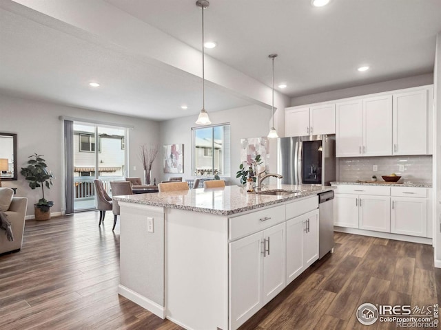 kitchen featuring stainless steel appliances, white cabinetry, a center island with sink, and decorative light fixtures